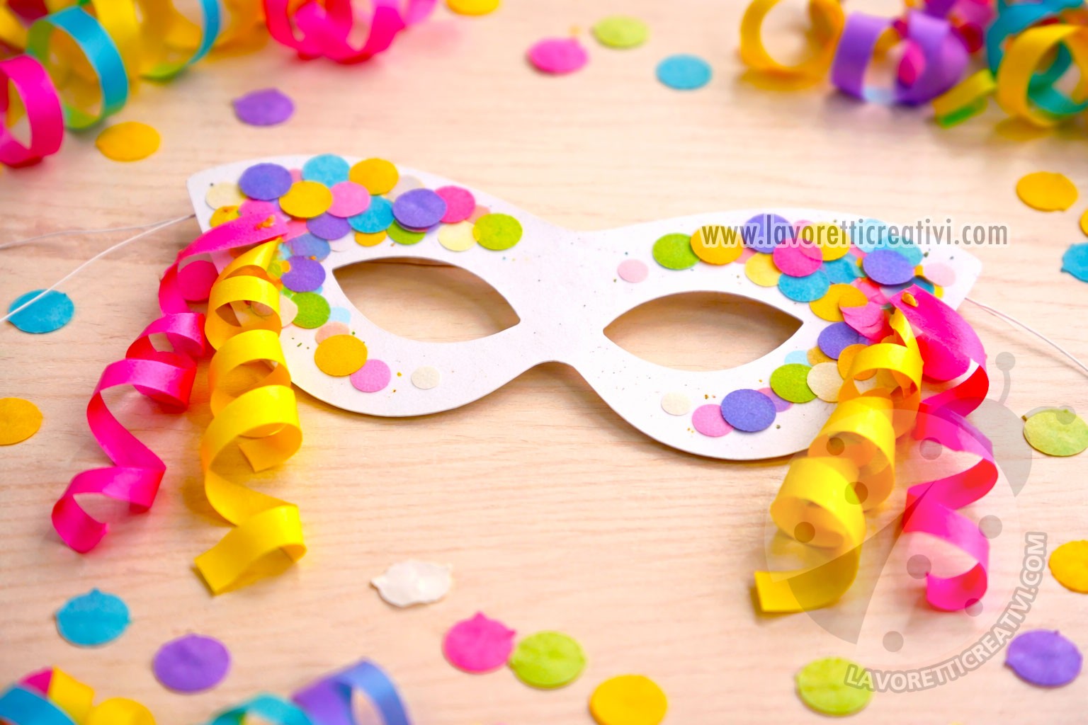 Maschera con coriandoli realizzata in cartoncino con decorazioni laterali di coriandoli e stelle filanti fissate che scendono verso il basso, lavoretto di Carnevale semplice per bambini.