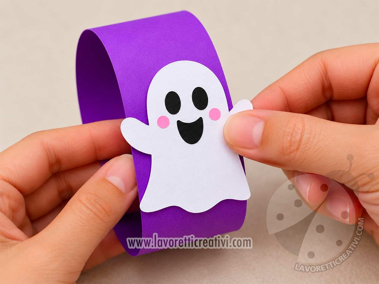 Festone di Halloween con Anelli di Carta 8 Mani che incollano un fantasmino di carta bianca su un anello viola per realizzare un festone di Halloween fai da te.